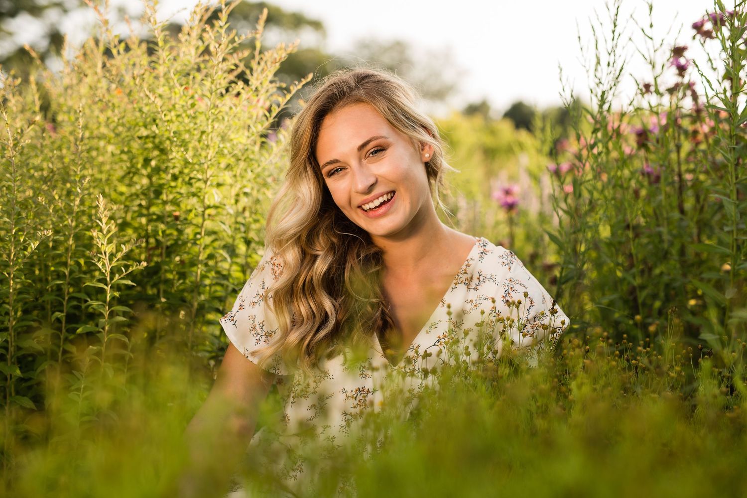 Person in white lace dress poses in a sunlit wildflower meadow during golden hour.