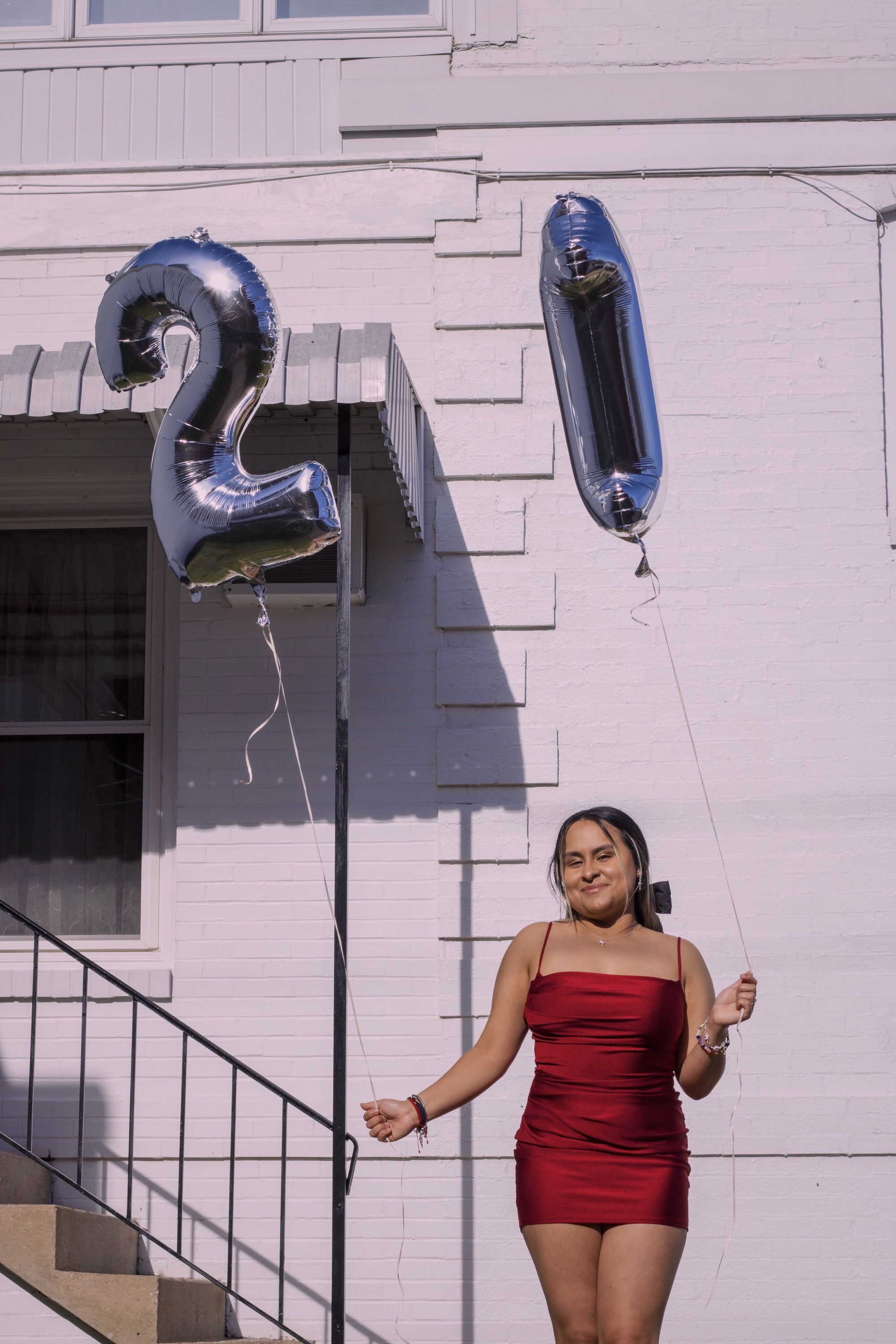 Young woman in a red dress holding birthday balloons and smiling in front of a vintage white building for her birthday