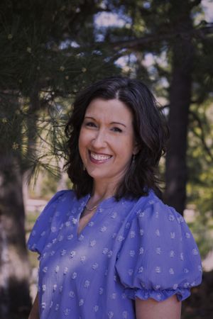 A woman smiling outside with trees in the background