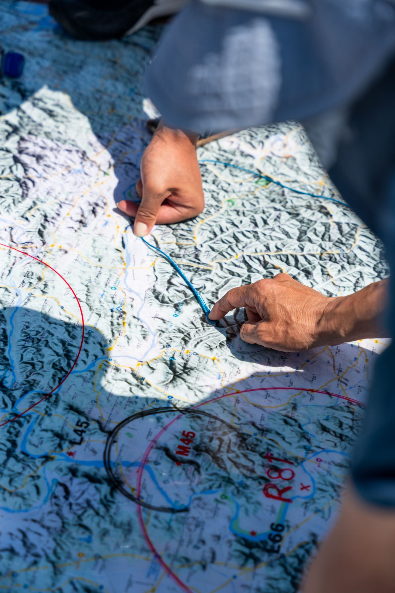 Hands pointing at locations on a detailed topographic map spread out on blue surface.