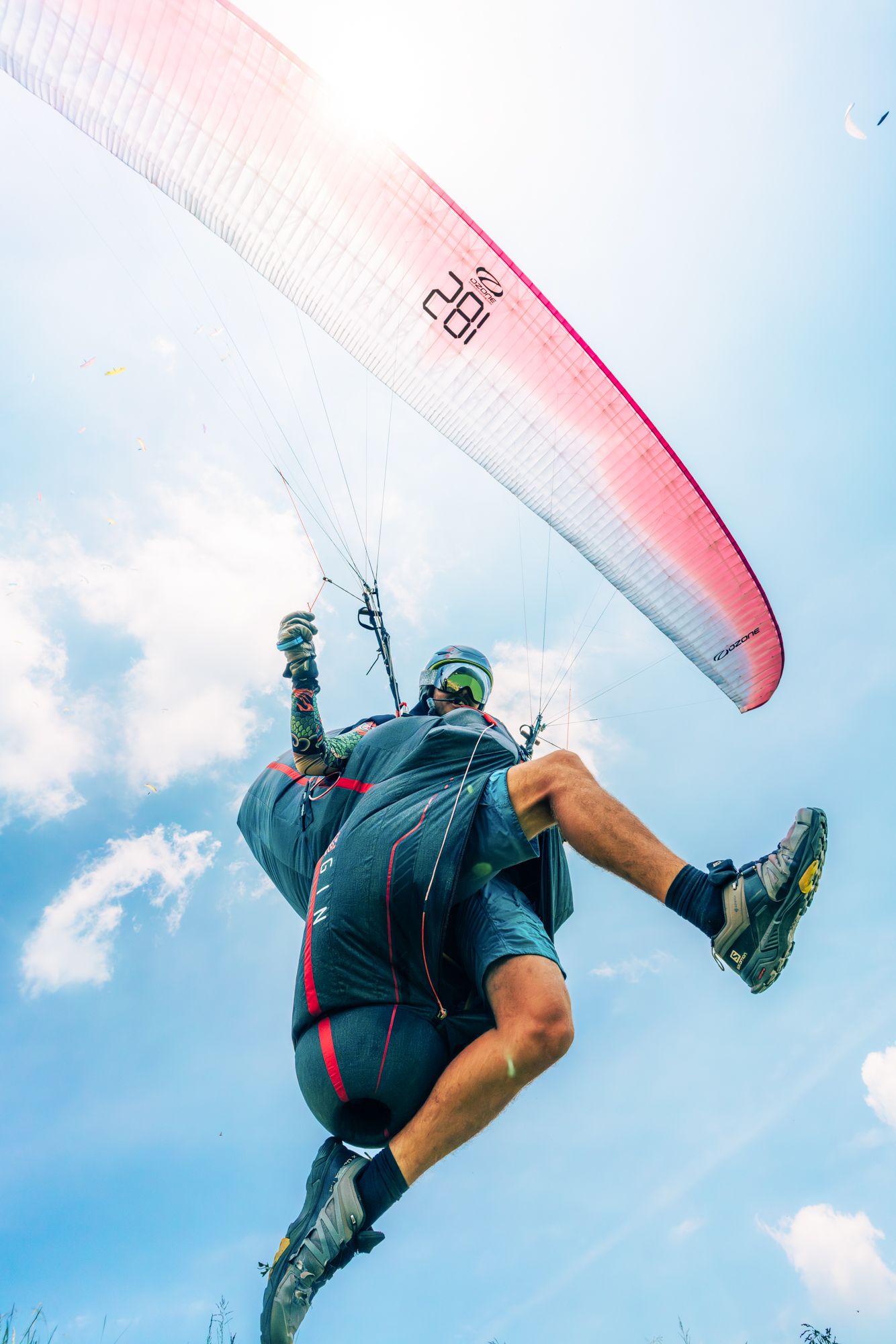 Low angle view of paraglider performing acrobatic maneuver with red and white wing against blue sky.