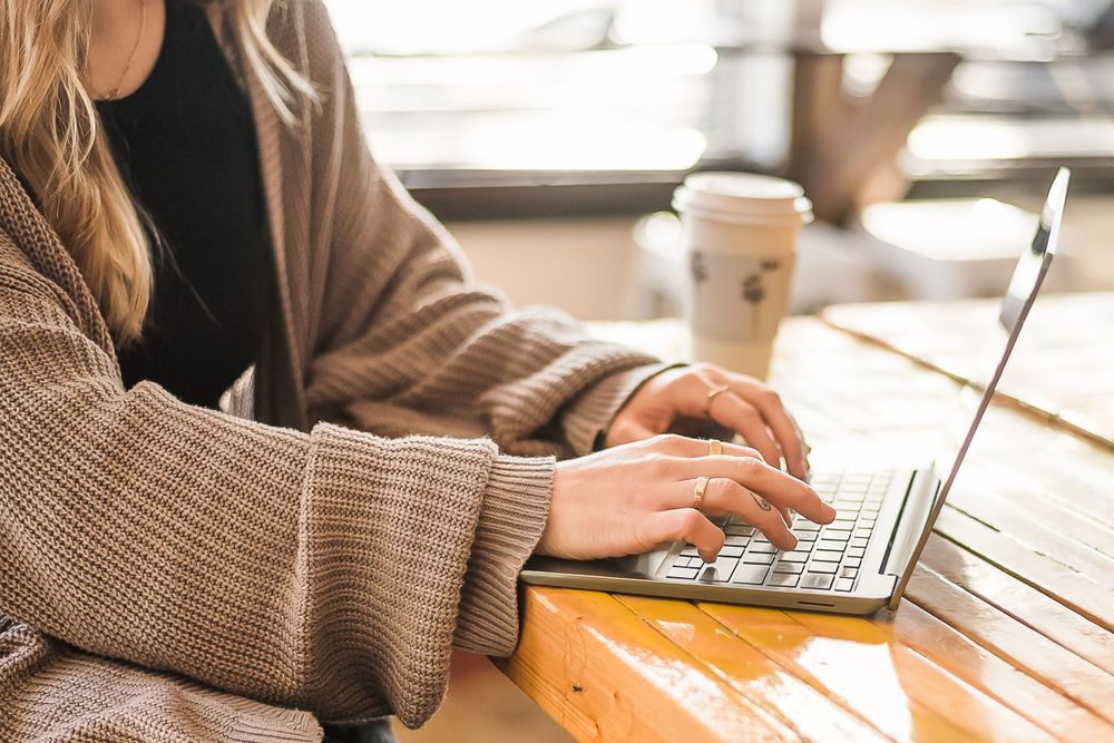 A close up image of a woman working on a computer at a wooden cafe table in White Rock, BC.
