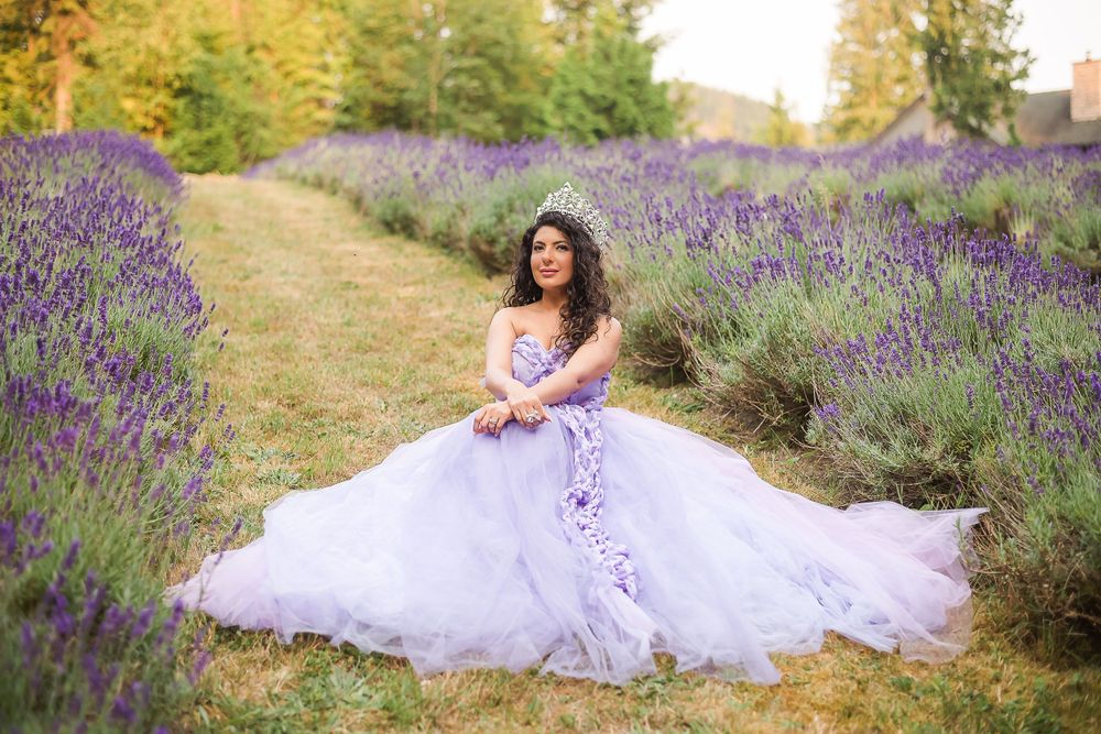 A beauty queen wears a stunning purple gown and her crown while she sits in a lavender field.