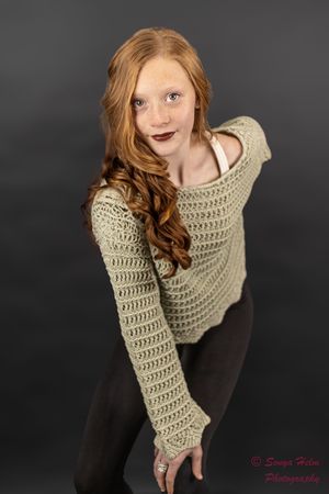 Artistic fashion portrait on dark background showing a person wearing a cozy beige knit sweater and dark pants.