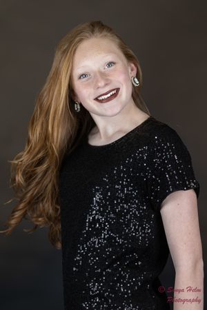 A smiling person wearing a sparkly black sequined top poses against a dark background.