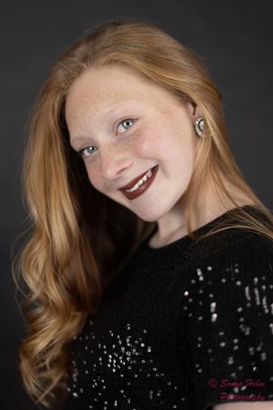 Portrait of a person with strawberry blonde hair wearing dark lipstick and a sequined black sweater against dark background.