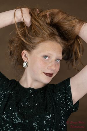 Portrait of someone in a sparkly black sequin top with tousled brown hair against a brown background.