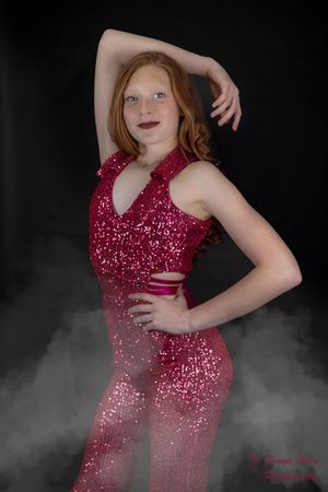 Dancer in a sparkly red performance outfit strikes a pose against dark backdrop with dramatic fog effects.