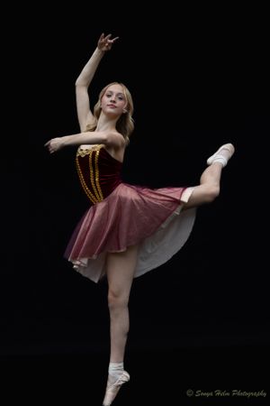A dancer in burgundy costume performs an elegant arabesque against black background. Sonya Helm Equine Photography, Bristol, TN