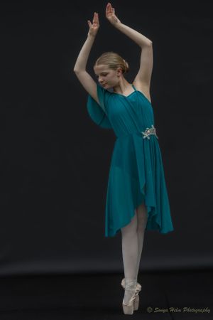 A ballet dancer in teal dress performs en pointe with raised arms against dark background. Sonya Helm Equine Photography, Bristol, TN