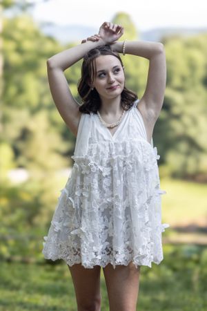 A person wearing a flowing white lace dress poses outdoors against a soft natural background in summertime.