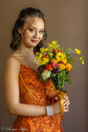 A formal portrait of someone in an orange sequined dress holding a vibrant bouquet of mixed flowers.