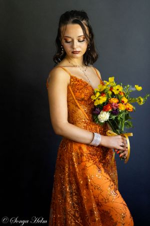 A dramatic portrait featuring someone in an orange sequined dress with a mixed flower bouquet.