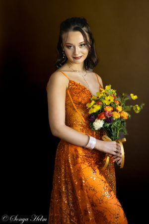 An elegant portrait of someone in a shimmering orange gown holding fresh flowers.