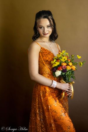 A portrait with someone wearing a sparkly orange gown while holding a colorful flower bouquet.