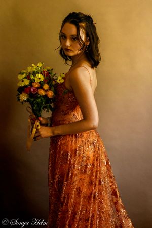 A moody side profile shot of someone in an orange sequined dress holding flowers.