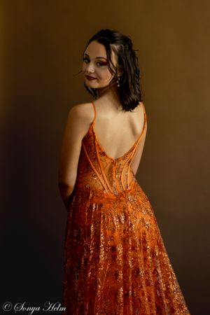 A back view portrait showing the detailed design of an orange sequined formal dress.