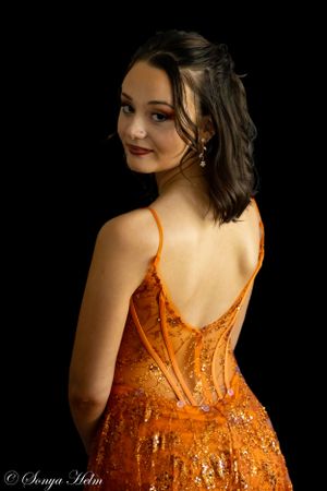 Portrait against black background showing backside detail of sequined orange evening gown.