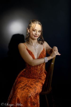 Dramatic studio portrait with spotlight effect showcasing orange sequined gown.