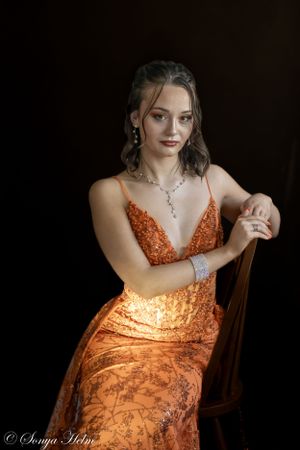 Glamorous portrait featuring sparkly orange dress and crystal necklace in moody lighting.