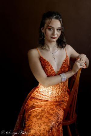 Studio portrait showcasing orange sequined formal dress and elegant jewelry.