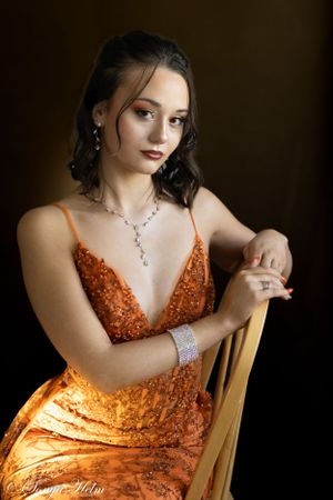 Elegant portrait featuring orange sequined gown and crystal jewelry against dark background.