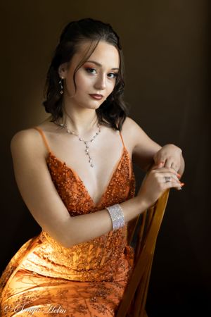 Studio portrait highlighting sparkly orange evening dress and delicate jewelry.