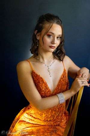 Dramatic portrait featuring orange sequined gown against deep blue background.