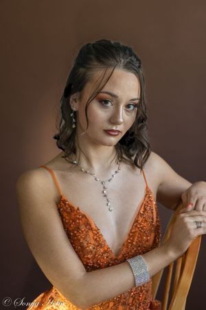 Elegant formal portrait featuring orange sequined dress against brown backdrop.