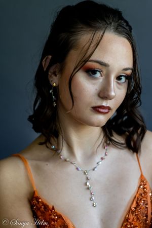Fashion portrait featuring model in sparkly orange dress with Y-necklace against dark background.