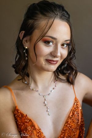 Soft beauty portrait highlighting wavy hairstyle and formal evening wear with statement necklace.