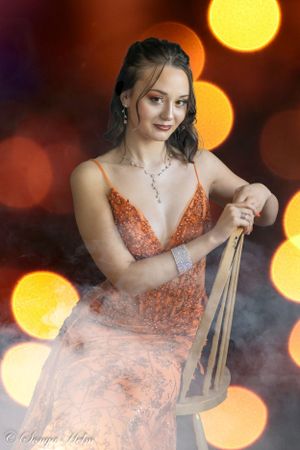 Dreamy portrait with bokeh lights featuring model in orange gown seated on chair.