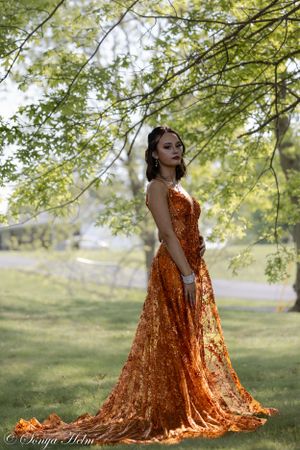 Long orange sequined dress flows gracefully against green garden backdrop.