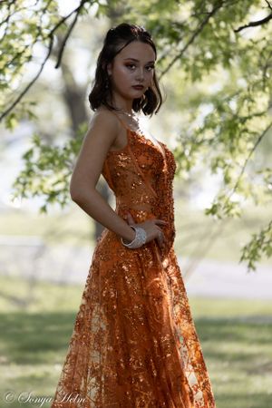 Shimmering orange formal dress captured in dreamy outdoor photography setting.