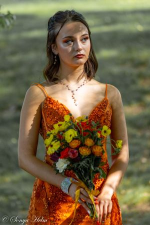 Elegant model poses with colorful bouquet while wearing sparkly orange evening gown.