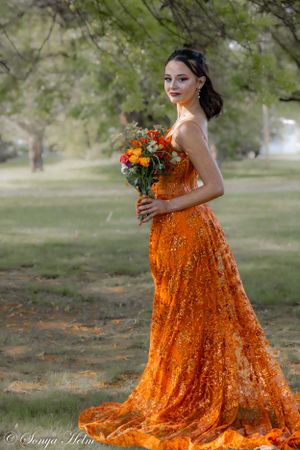 Flowing orange sequin dress complemented by vibrant fall flower bouquet in park setting.