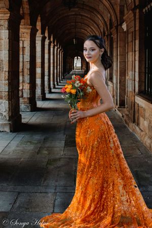 Stunning orange sequin gown photographed in historic stone archway corridor.