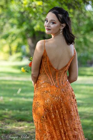 Detailed back view of orange evening gown with delicate strap design against green foliage.
