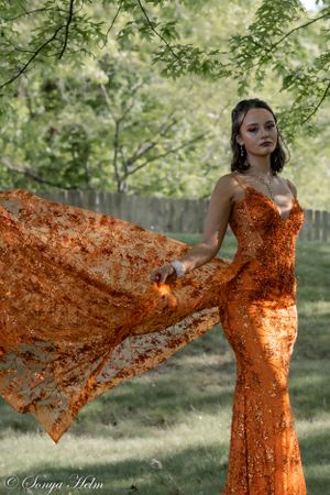 A stunning orange sequined gown with flowing fabric photographed in a lush garden setting.