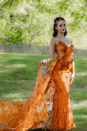 An elegant orange sequined evening gown with flowing train captured in an outdoor garden.