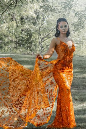 An elegant orange sequined dress with dramatic train captured in a garden setting.