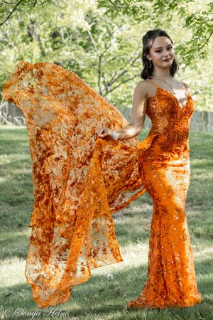 A sleek orange sequined dress with flowing panels photographed in natural outdoor lighting.
