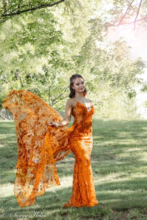A glamorous orange sequined dress photographed in soft natural lighting under trees.
