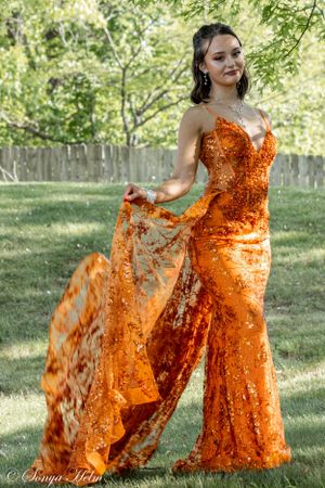 An elegant orange sequined gown with dramatic flowing fabric captured in a garden.