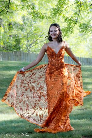 An elegant orange sequined gown flows in motion against a sunlit garden backdrop.