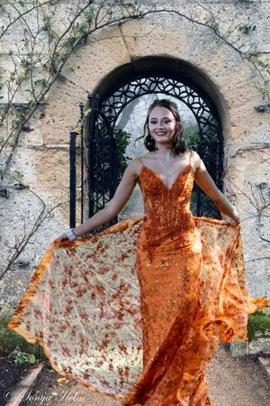 A sparkly orange evening dress photographed in front of an ornate stone archway.
