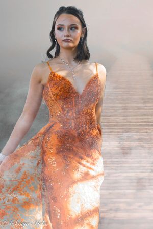 A shimmering coral formal dress catches the light in a dreamy outdoor setting.