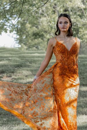 A form-fitting orange sequined dress flows elegantly in an outdoor photoshoot.