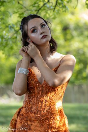 An elegant pose in a fitted orange sequined gown showcased in natural lighting.