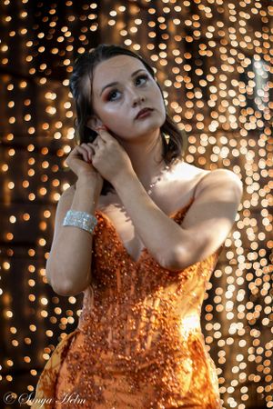 A glamorous orange dress sparkles against a backdrop of bokeh lights.